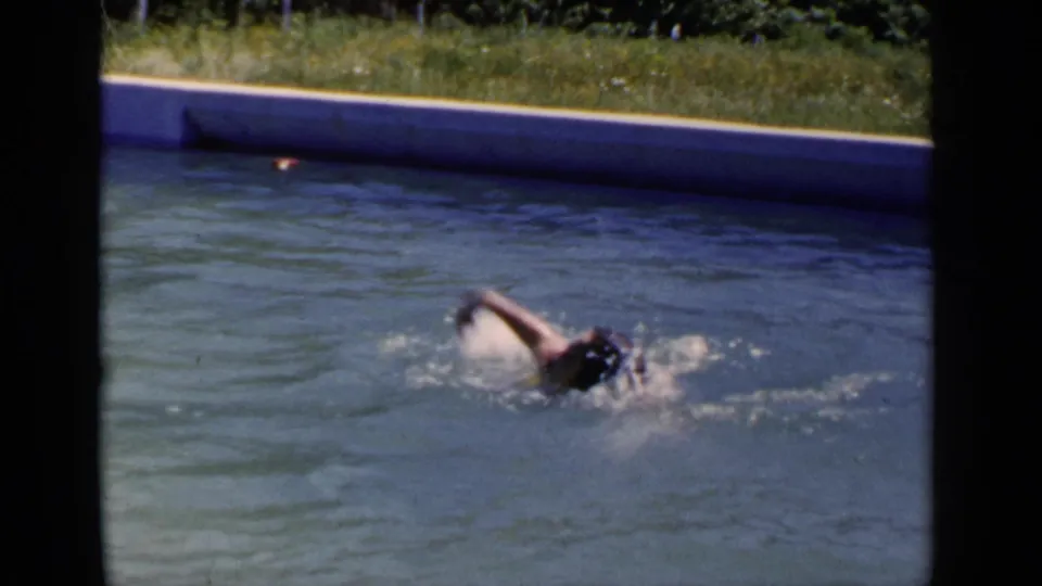 1951 New York 8mm frame showing the swimmer turning into a stroke, with splashing water and a grassy poolside background.