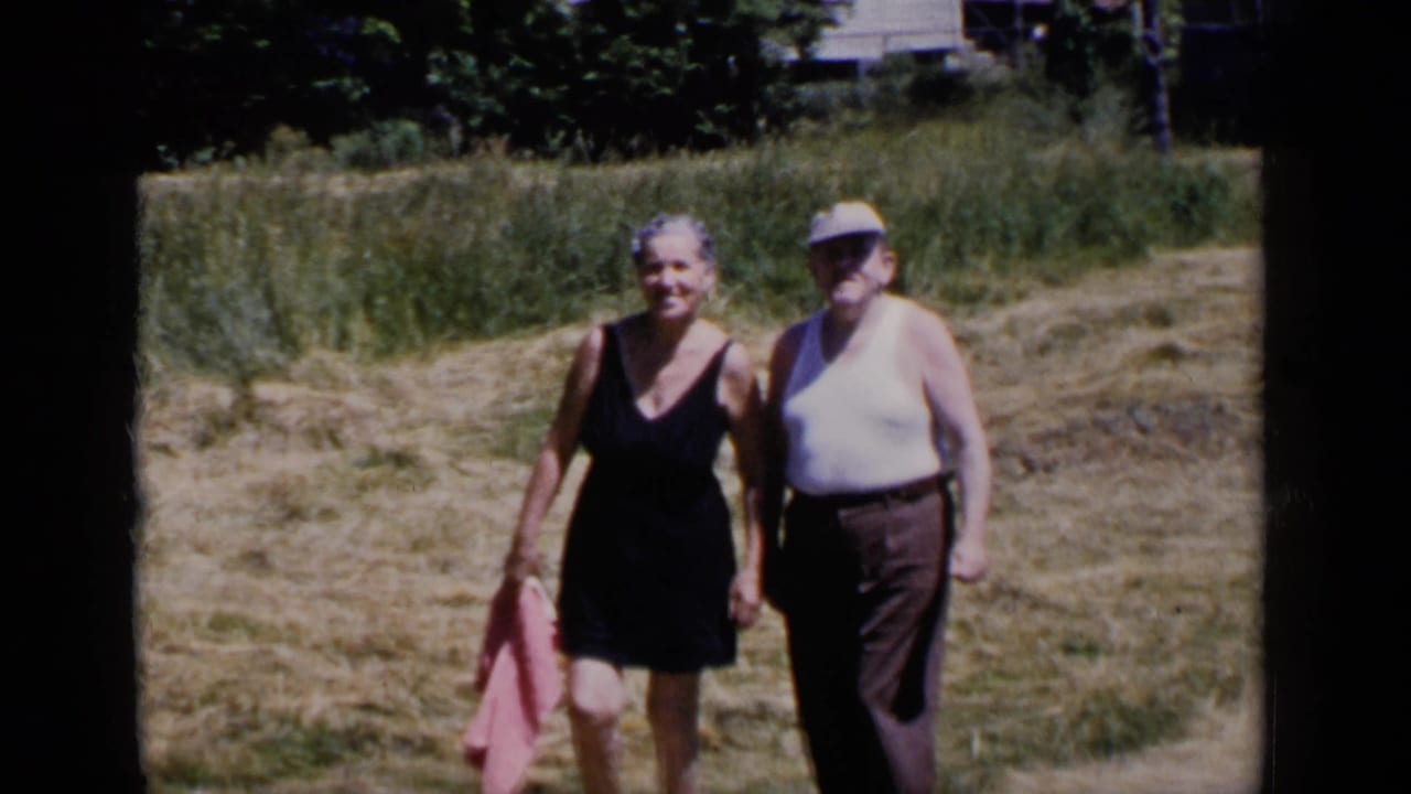 Older couple walking toward the camera through dry grass beside taller field growth.
