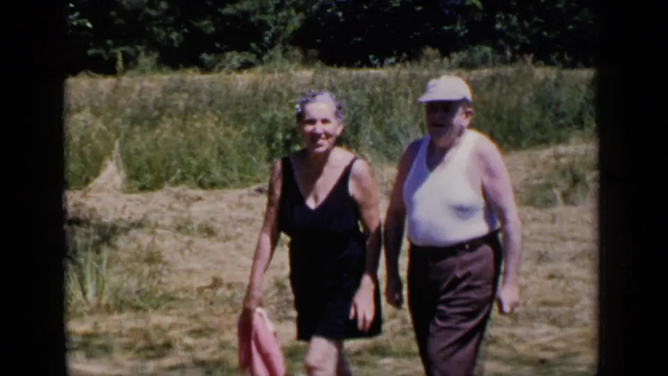 Near the end of the clip, the older woman and man are close to the camera in the bright field, still framed as informal home-movie subjects.