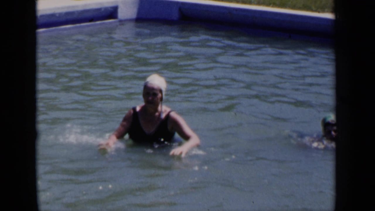 A woman in a white swim cap and dark swimsuit faces the camera while standing in a New York pool in 1951 footage.