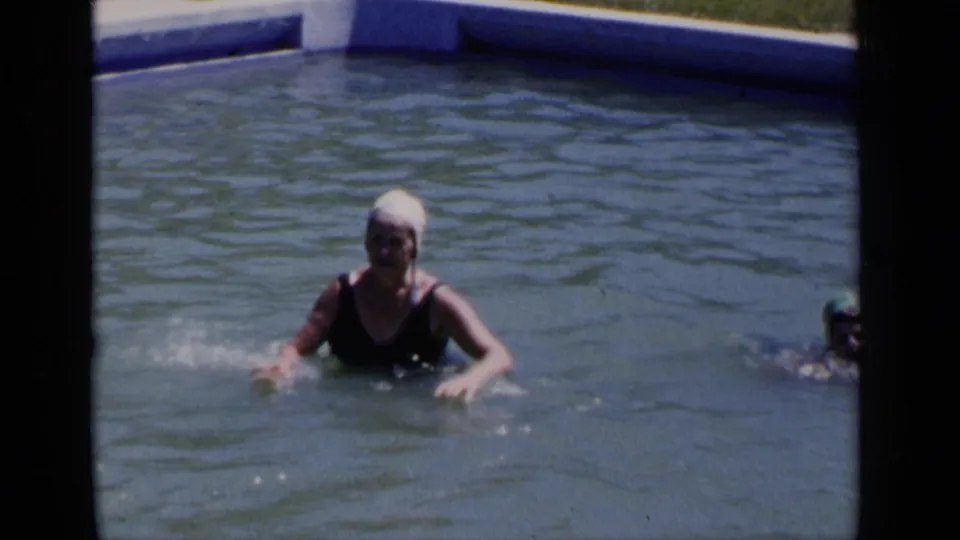 A woman in a white swim cap and dark swimsuit faces the camera while standing in a New York pool in 1951 footage.
