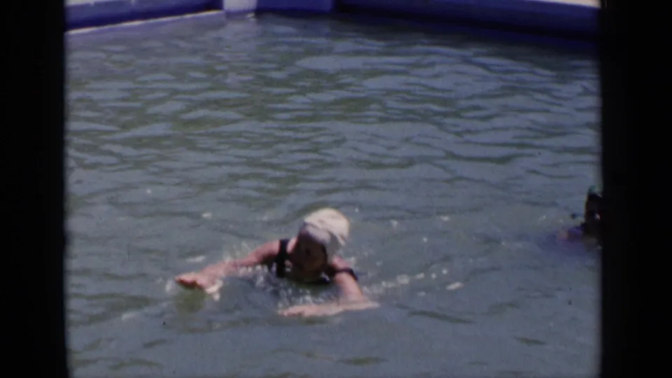 The woman swims through the outdoor pool in 1951 New York home-movie footage, with another swimmer partly visible at right.