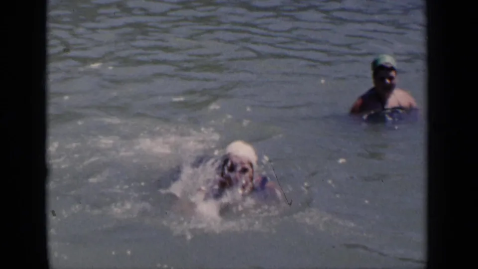 A swimmer splashes forward in the pool as another capped swimmer watches from the background in 1951 New York footage.