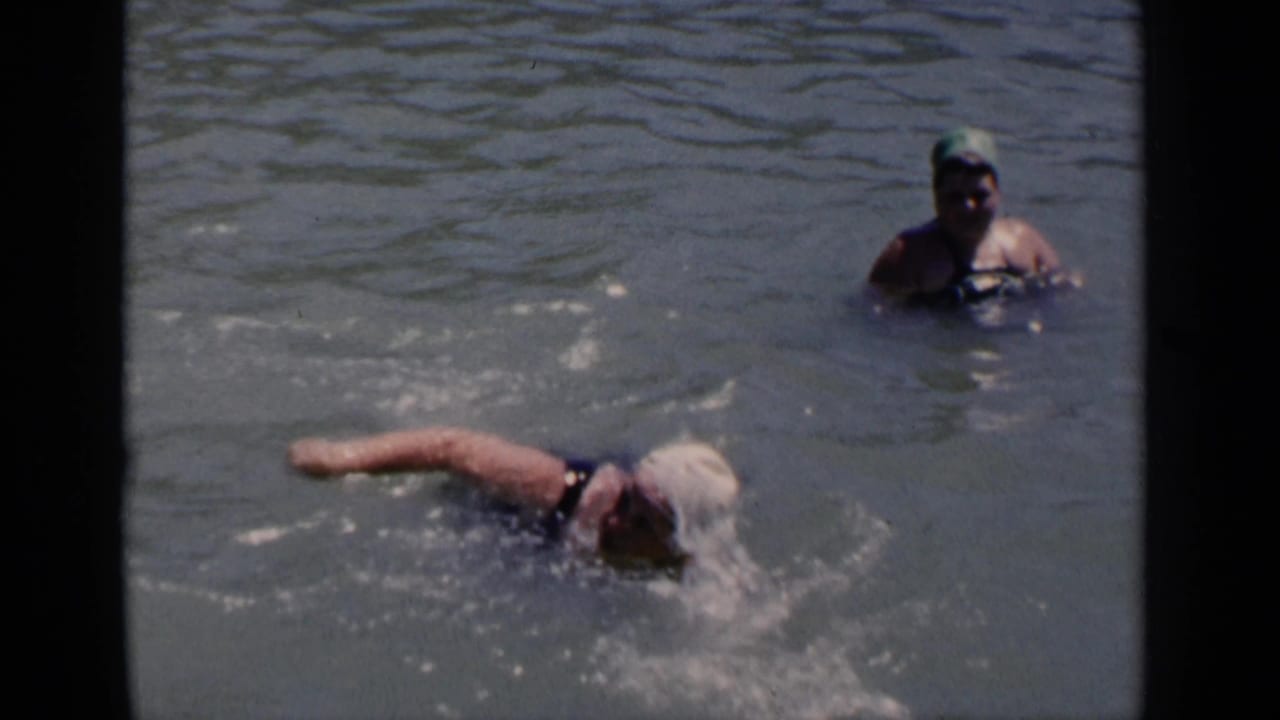 1951 New York 8mm frame showing a woman in a white swim cap swimming in open water as another person in a green cap observes.