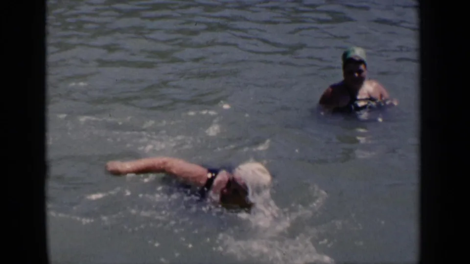 1951 New York 8mm frame showing a woman in a white swim cap swimming in open water as another person in a green cap observes.