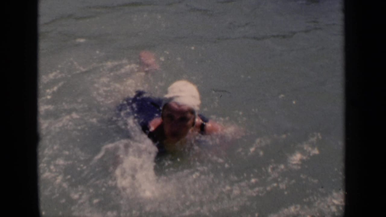 Woman in a white swim cap swims through rippled open water.