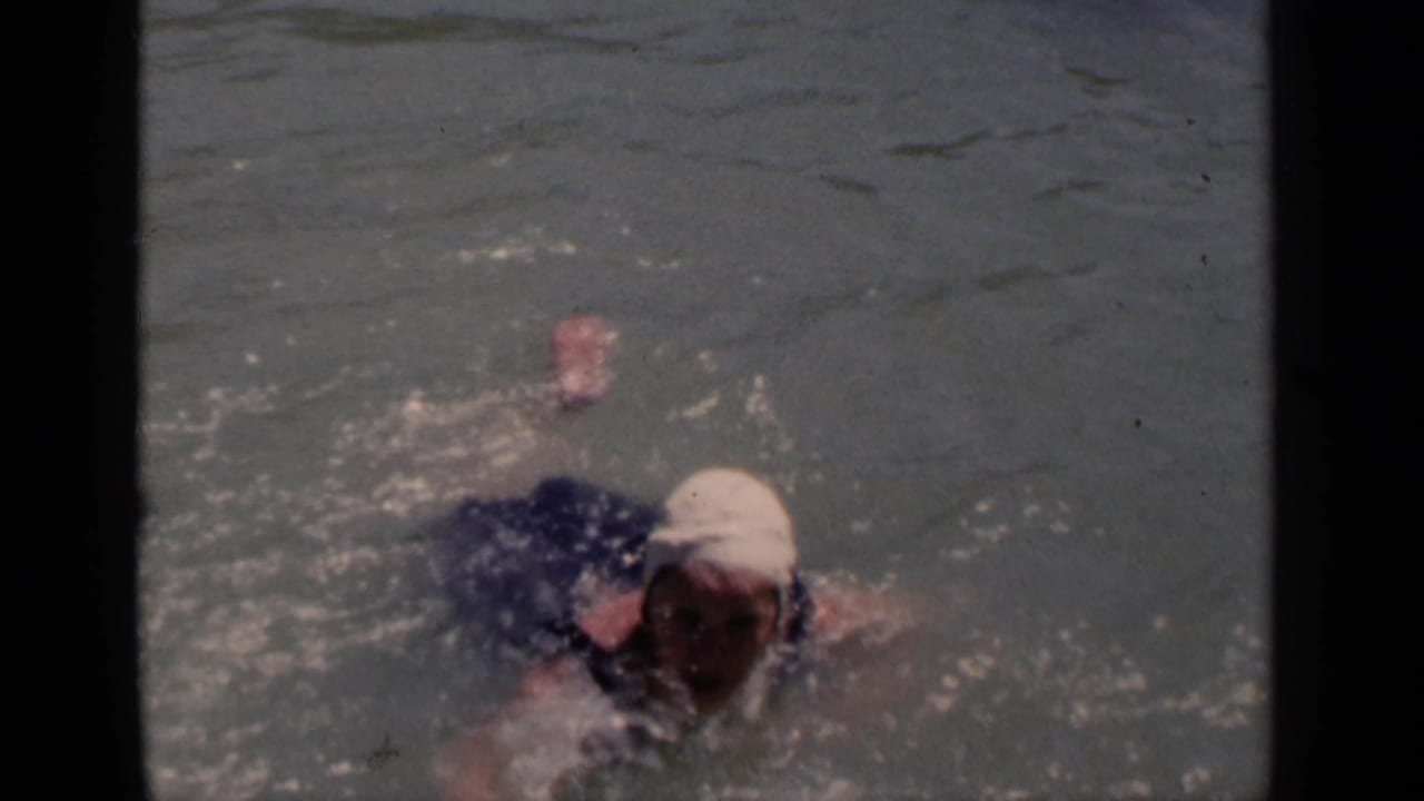 Woman swimmer raises an arm while moving across open water.
