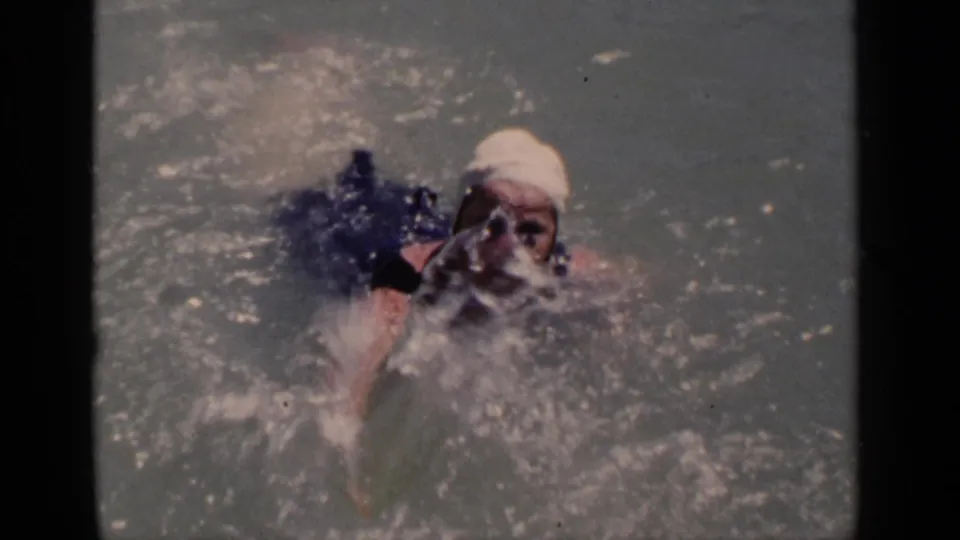 1951 New York 8mm still of a woman in a white swim cap and dark one-piece bathing suit swimming toward the camera in a lake.