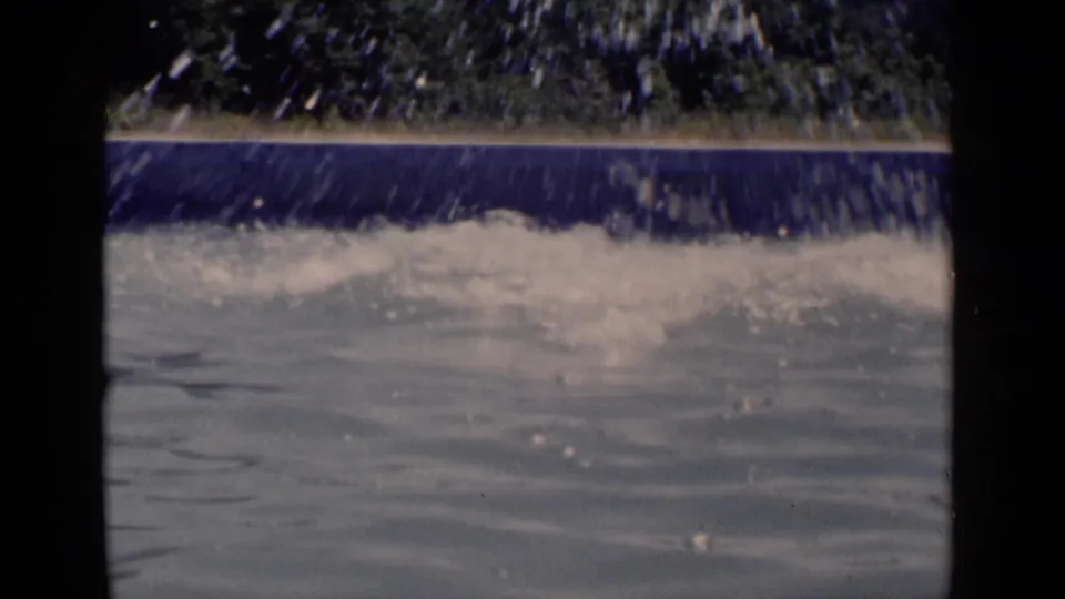 1951 New York home-movie frame showing a large splash in a sunlit pool near a blue rim and trees.