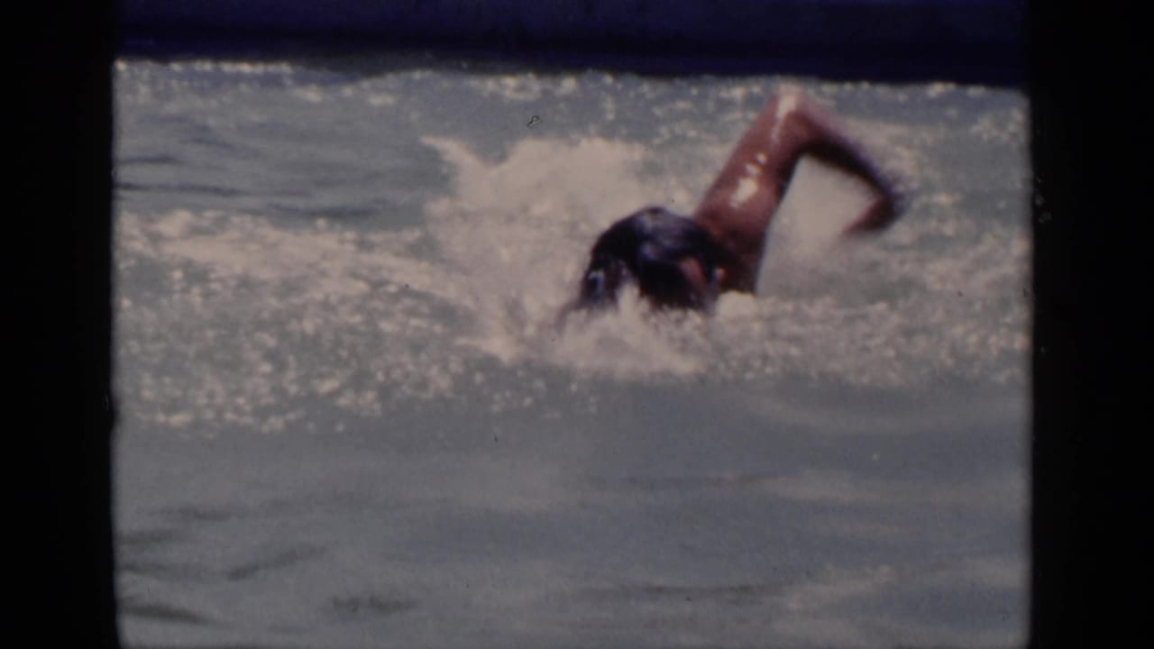 Swimmer in a pool performs freestyle with one arm raised above the water.