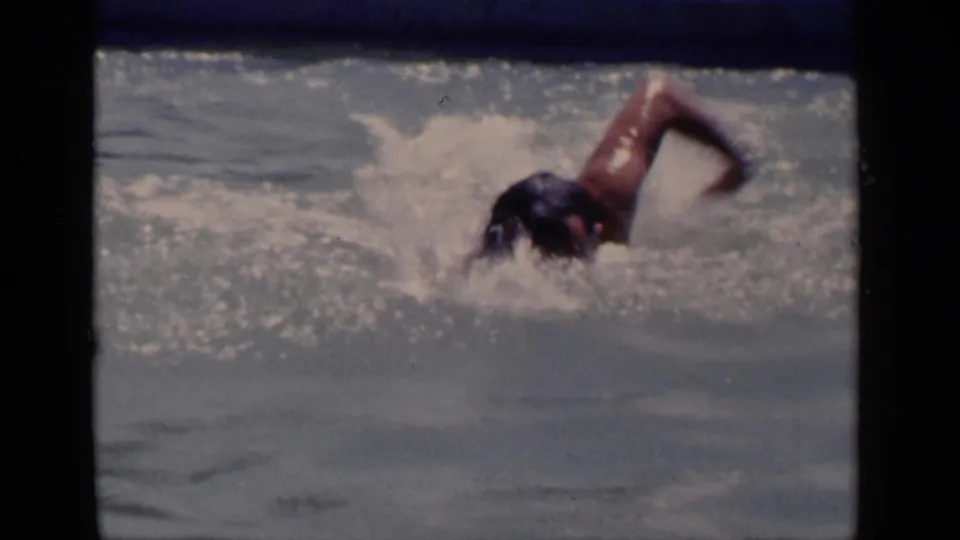 Swimmer moves through a sunlit pool in the supplied 1951 New York home-movie footage, with water splashing around the head and arm.