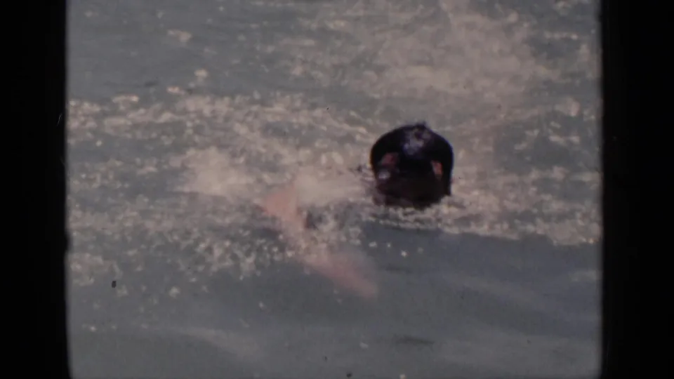 Swimmer faces the camera while moving through a sunlit pool, with the 8mm frame showing soft focus and water glare.