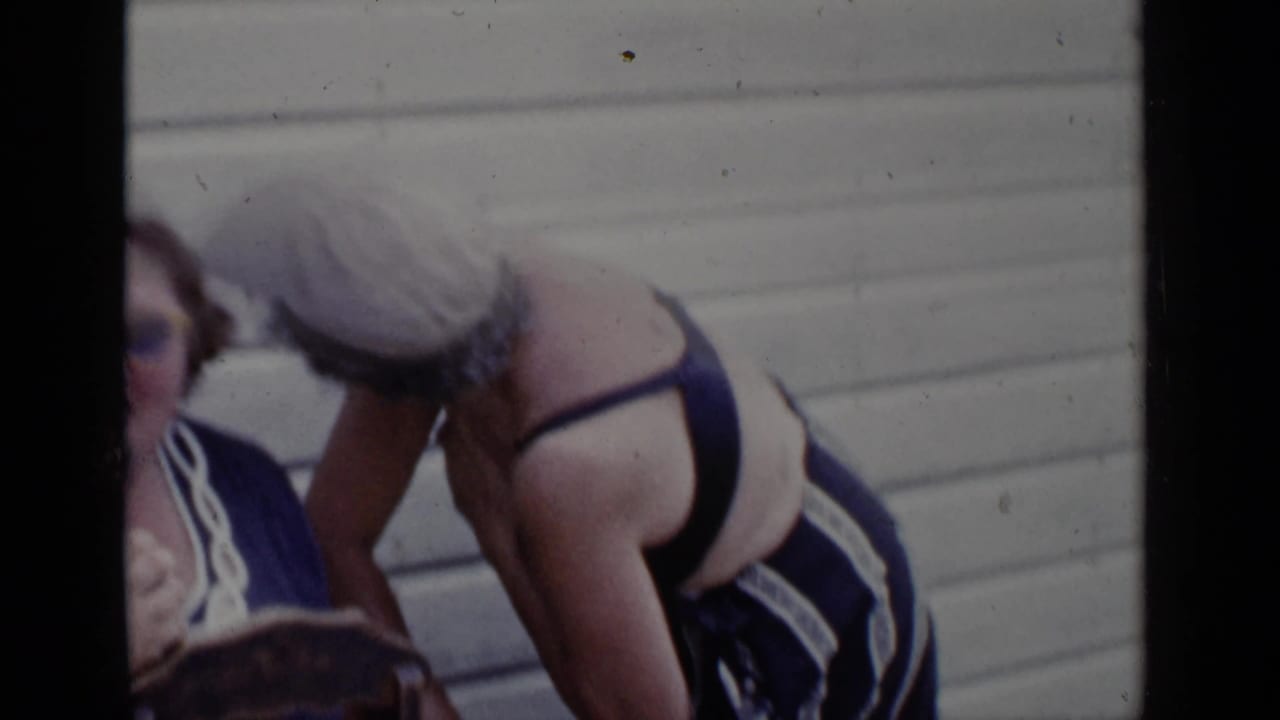 Woman in a sun hat bends toward a seated woman near light-colored exterior siding.