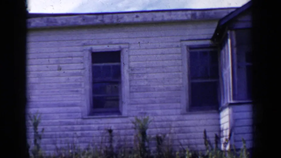 A closer 8mm view shows the white clapboard house, windows, porch edge, and plants near the foundation in the 1951 New York footage.