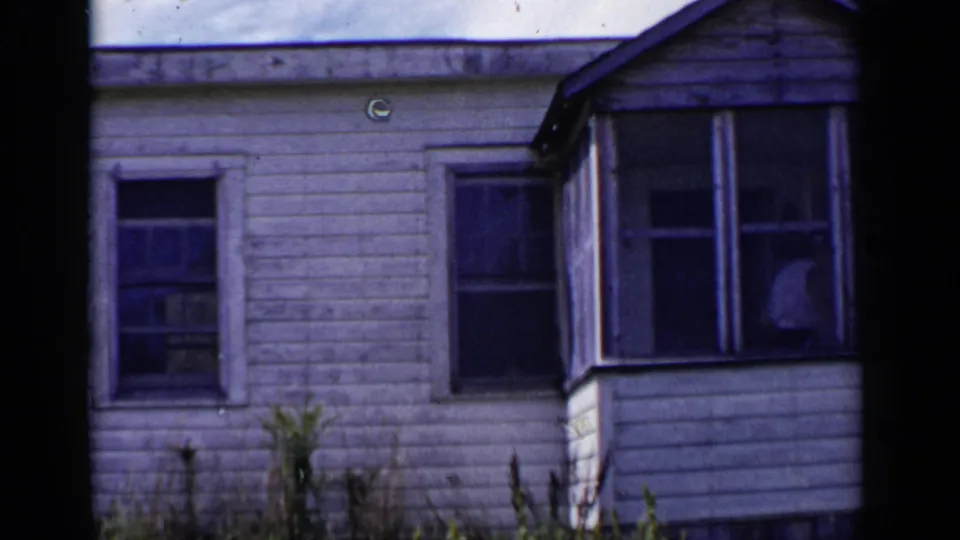 1951 New York home-movie frame showing a weathered white clapboard house with screened porch and dark window curtains.