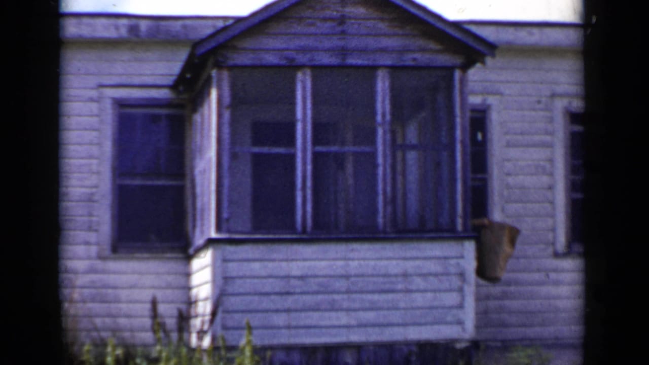 White house facade with screened porch, windows, and a paper bag at the right edge.
