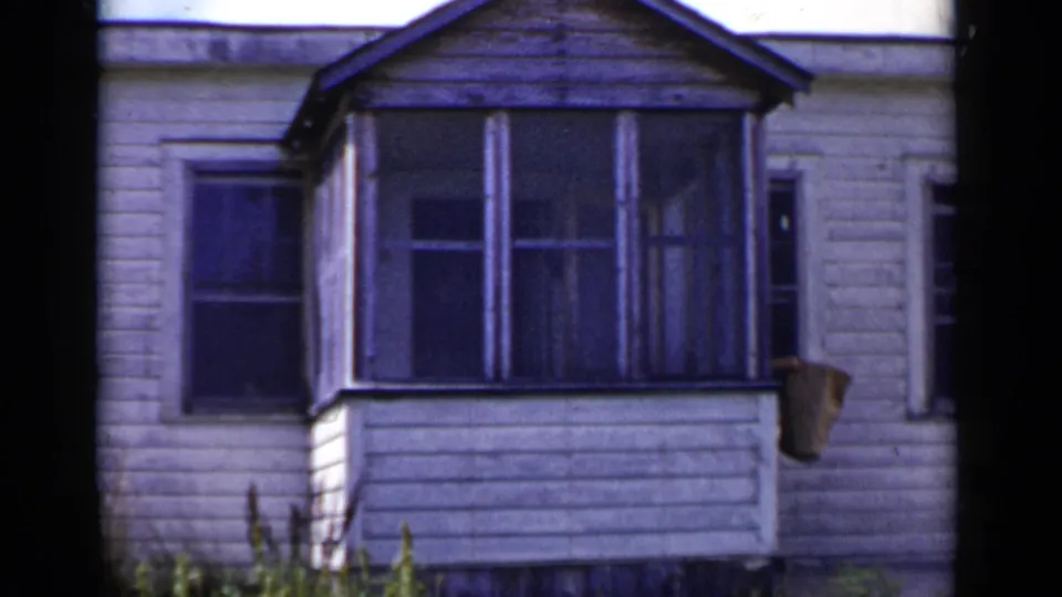 1951 New York home-movie frame of the same white house exterior, with porch windows and an object near the right side.