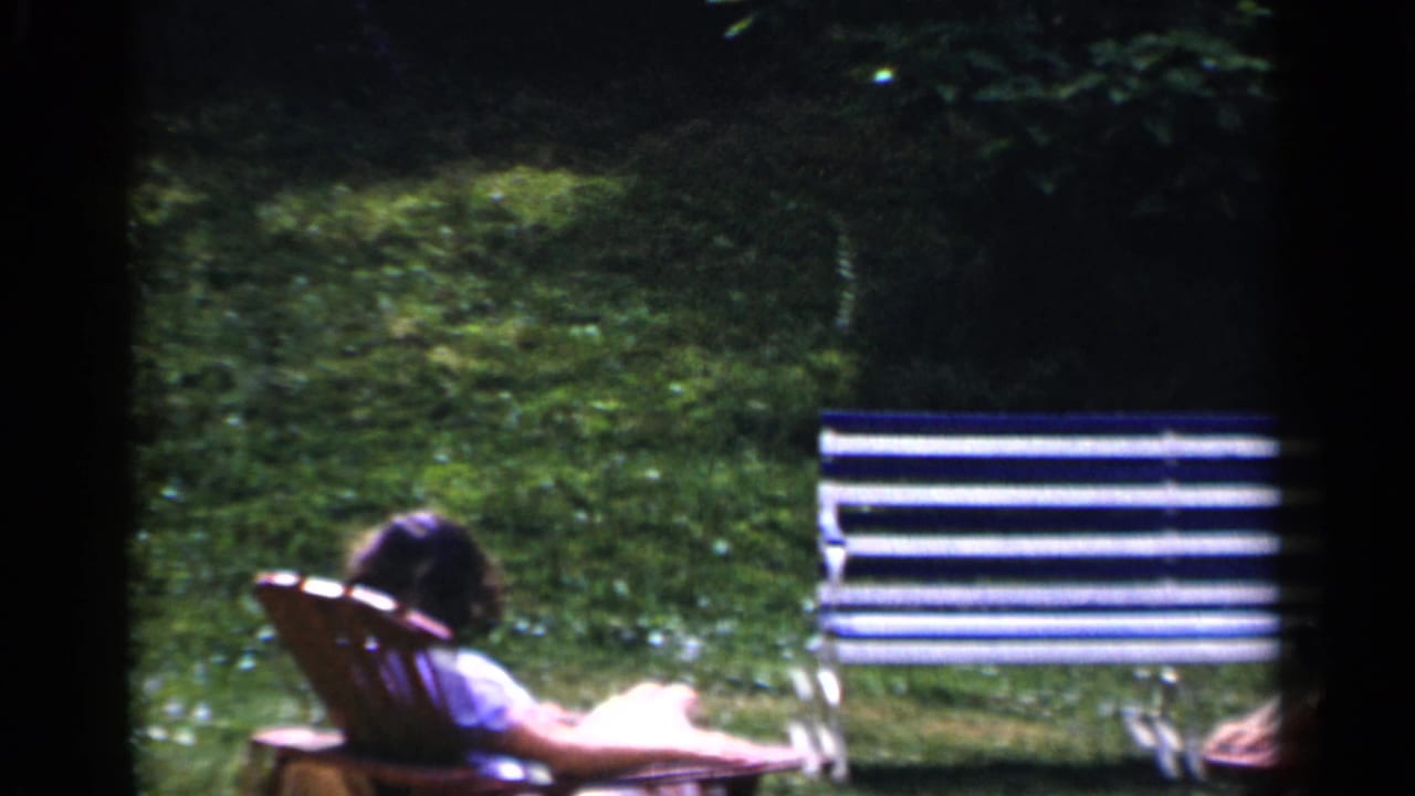 Woman reclining in a lawn chair beside a striped bench on a grassy yard.
