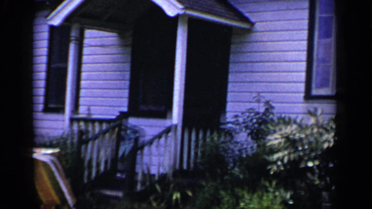 Front porch of a white clapboard house with railings, shrubs, and a striped lawn chair at the edge.