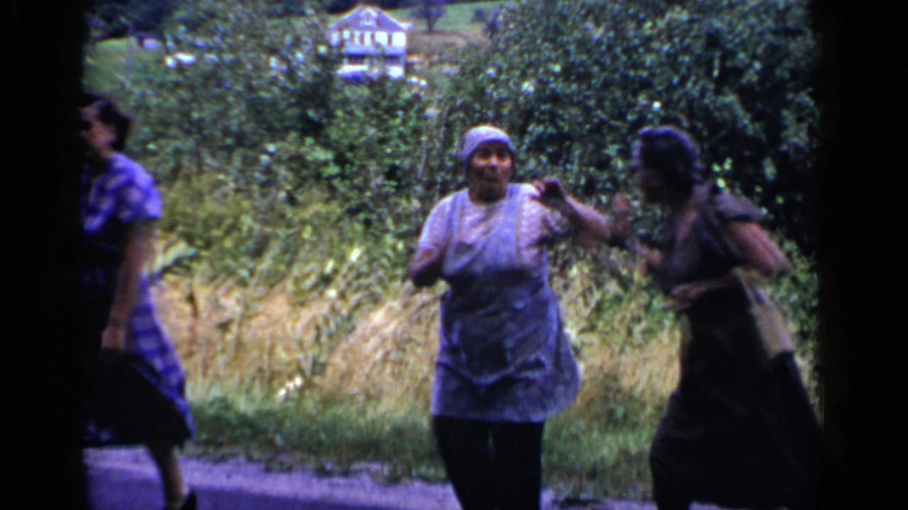 Three adult women near a rural road with trees and a distant house behind them.