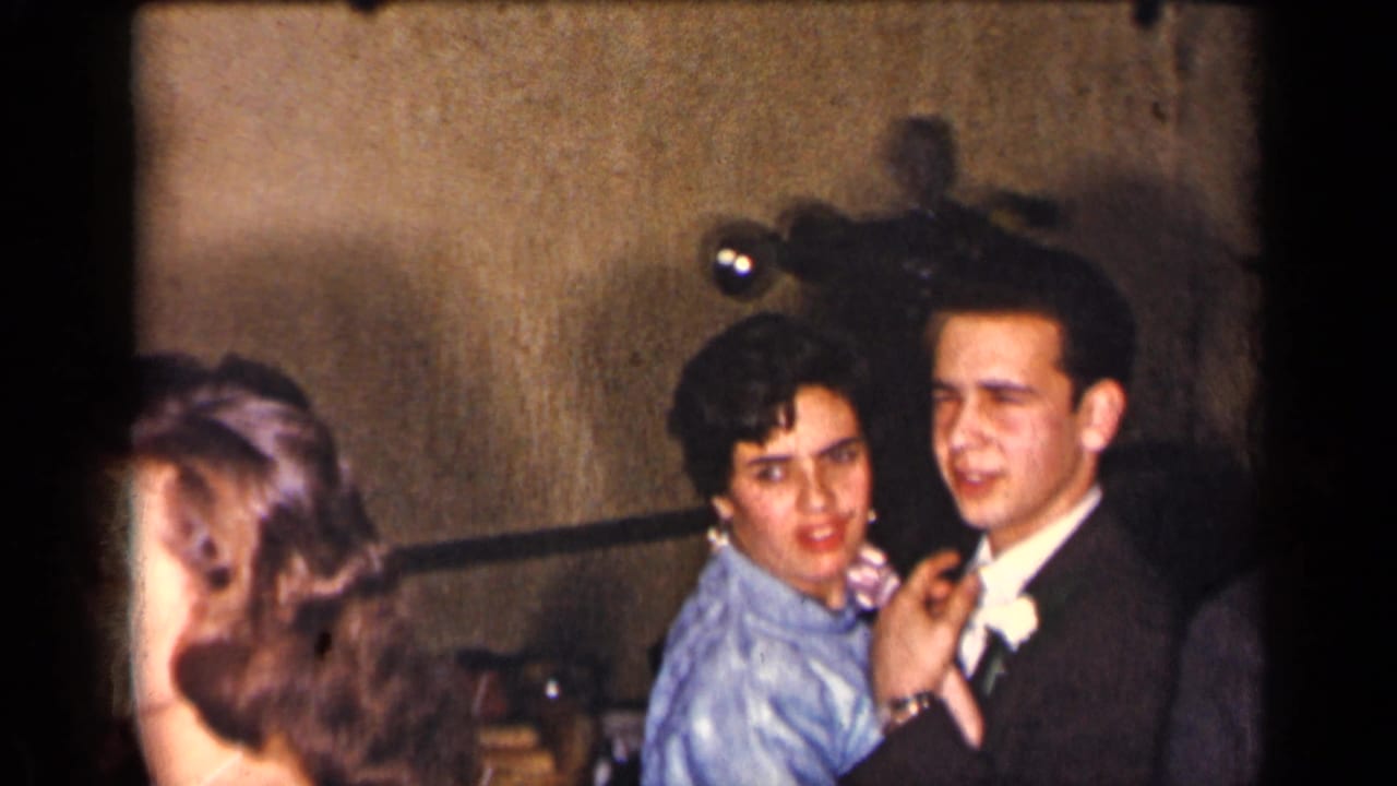 Young couple dancing at a formal indoor party as other guests stand nearby.