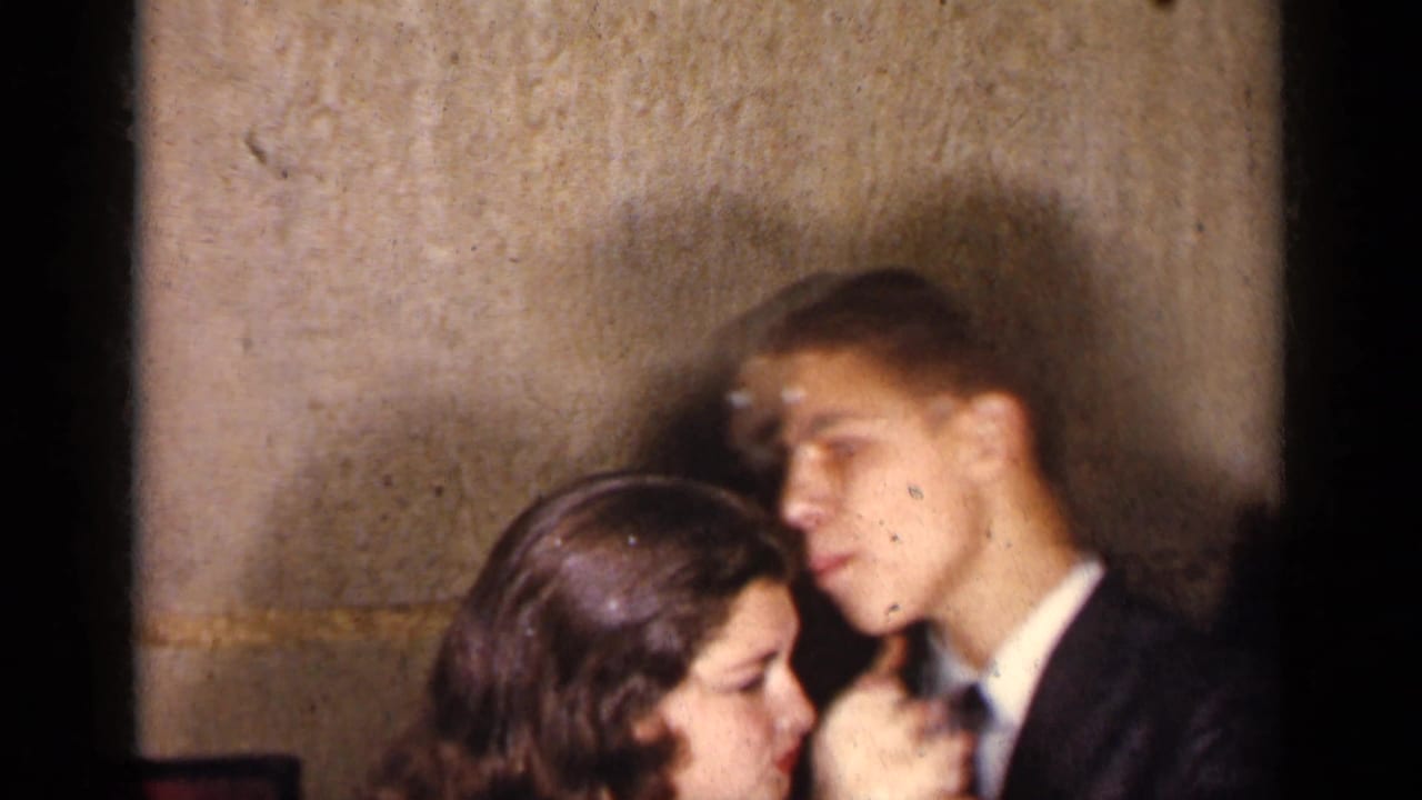 Couple dancing closely beside a textured wall during an indoor social.
