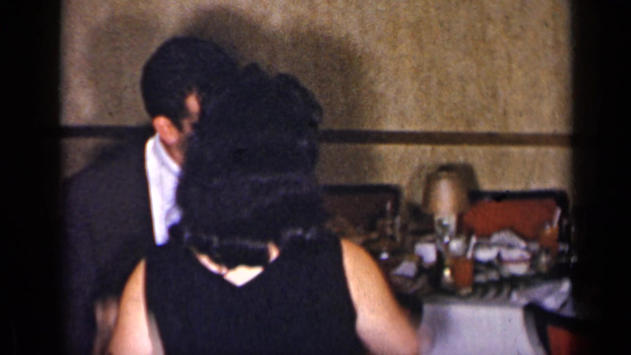 Couple dancing beside set tables in a dim interior.