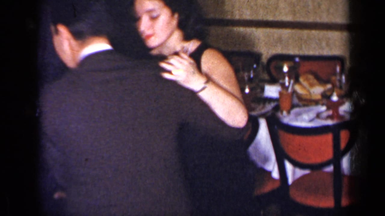 Woman in a dark dress dances with a suited man near a table.