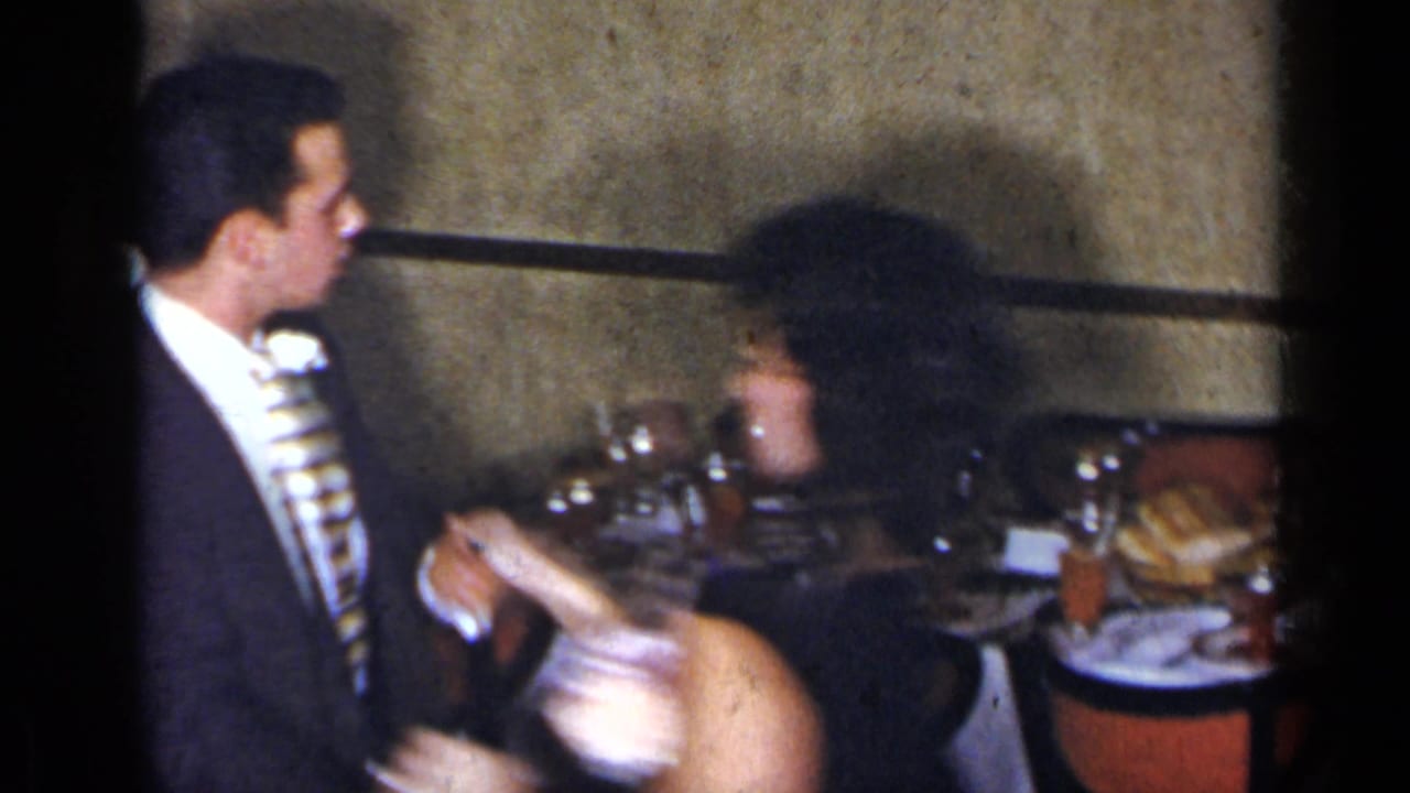 Man in a dark suit sits beside a woman in a black dress at a dinner table.