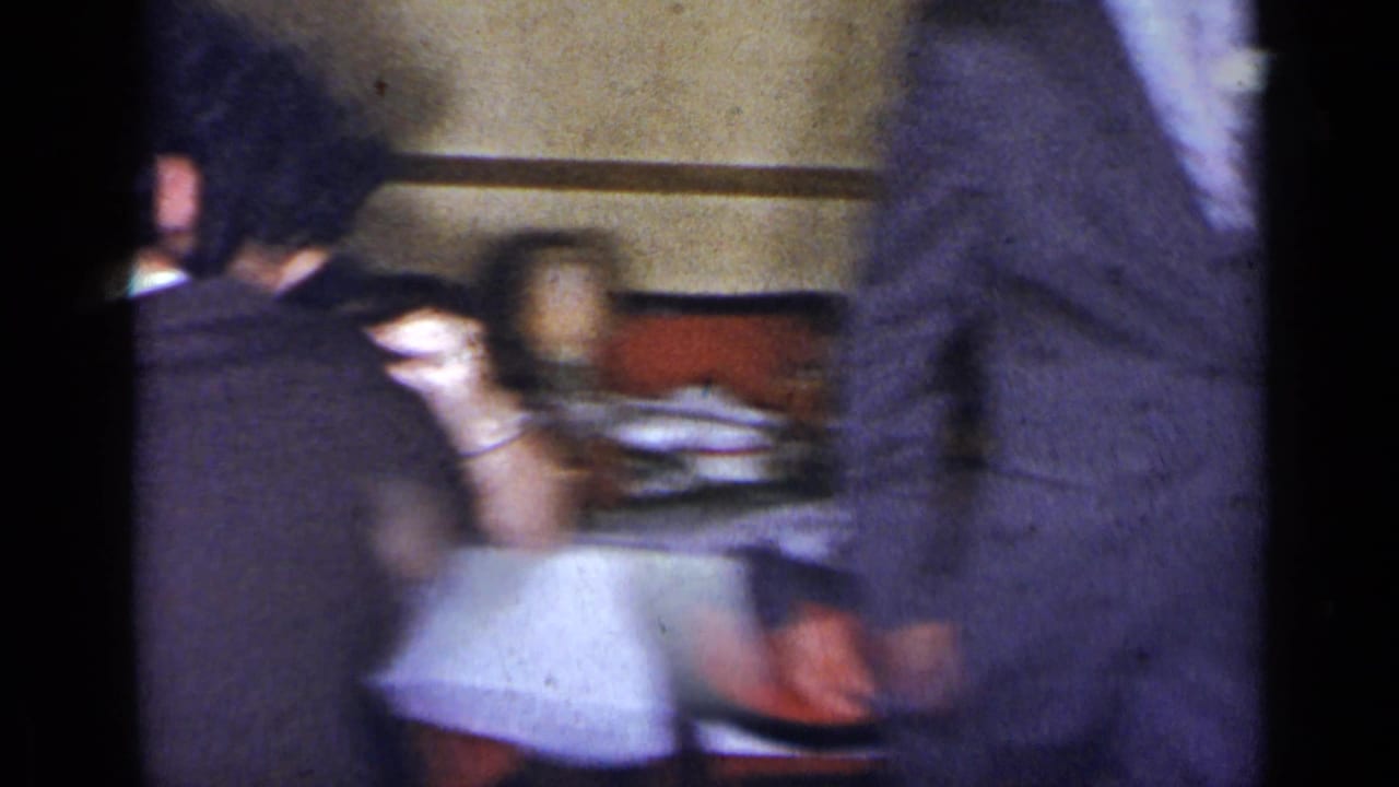 Handheld 1954 New York home-movie frame showing blurred guests around a formal dinner table in a private interior.