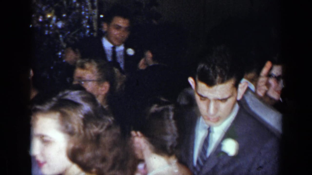 Young man in a suit with a white boutonniere moves through a crowded formal party.