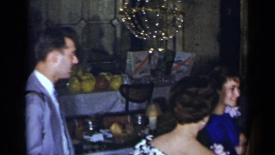 A buffet table with fruit and drinks sits beneath a chandelier as formally dressed guests pass through the New York party interior.