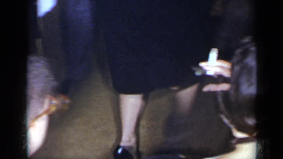 1954 New York home-movie frame showing a woman holding a cigarette among adults at an indoor party.