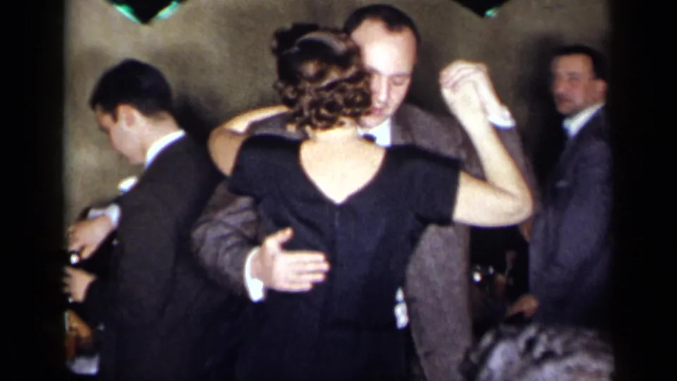 1954 New York home-movie frame of a couple dancing at a formal indoor party, with guests and table settings in the background.