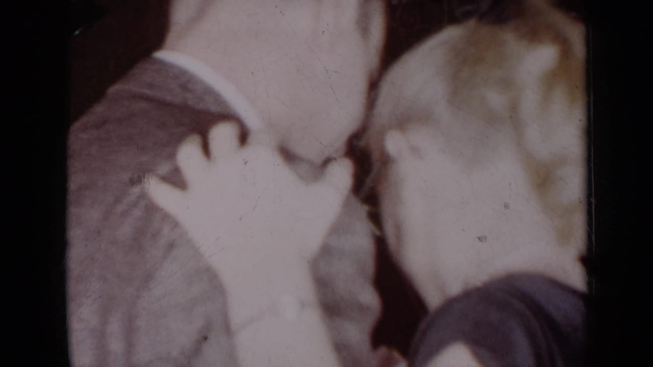 A light-haired woman places her hand on a suited man’s shoulder during a close embrace.