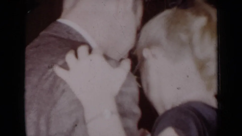 The 1954 New York home-movie frame shows a woman’s hand on a suited man’s shoulder as the couple stands very close indoors.