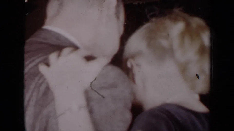 This 1954 New York 8mm frame shows the couple close together, with the man’s suit back and the woman’s profile visible in soft indoor light.