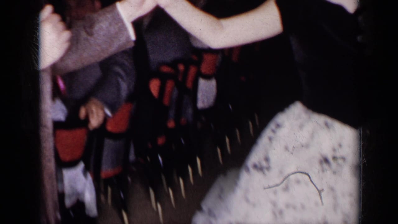 Cropped party view with dancers' arms, suits, a patterned skirt, and nearby guests in dim light.