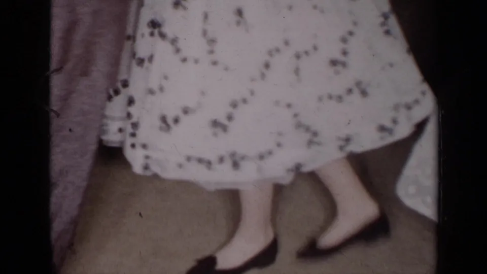 Lower-body 8mm frame from the New York dance scene, focused on the woman's patterned skirt and shoes as the couple steps.