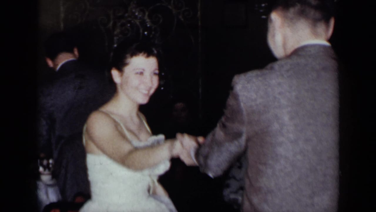 Young woman in a white dress dances with a man in a suit at a dim party.