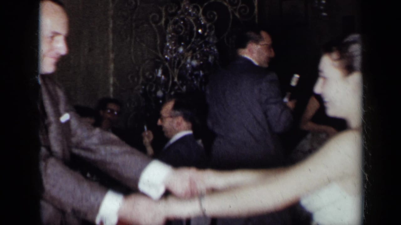 A suited man and woman dance close to the camera at the 1954 New York party, with seated guests and table settings behind them.