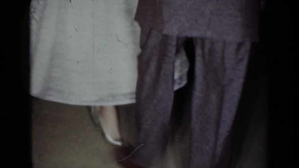 1954 New York home-movie frame showing cropped lower bodies of wedding guests or dancers in formal clothing.