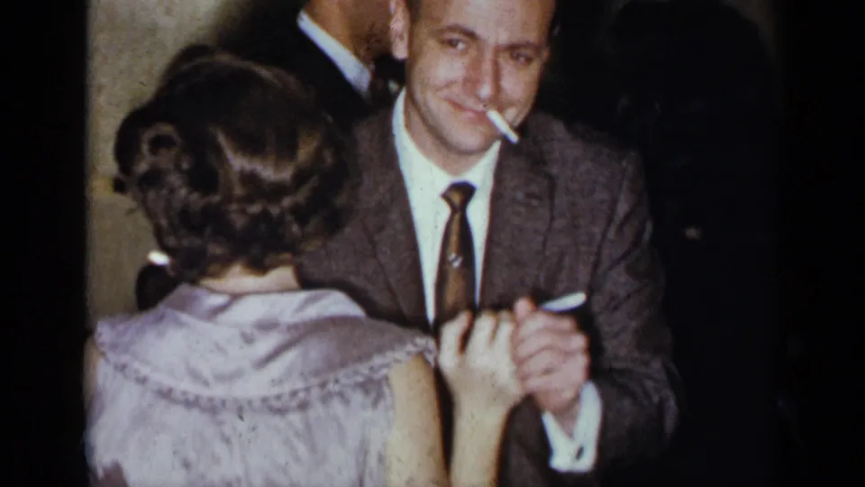 At the 1954 New York gathering, the smoking man in a brown suit smiles while dancing with the woman in a light purple dress.