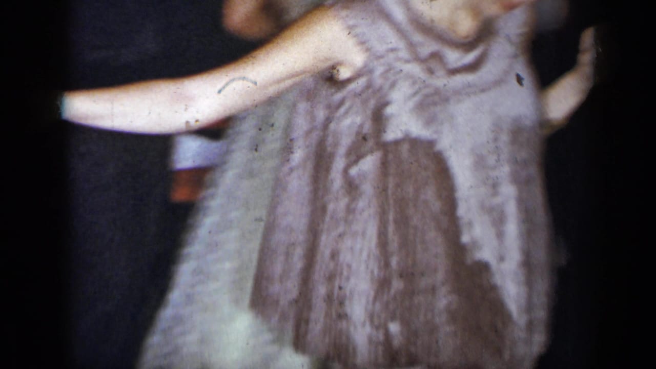 1954 New York home-movie frame of a woman in a light sleeveless dress extending her arm while dancing among party guests.