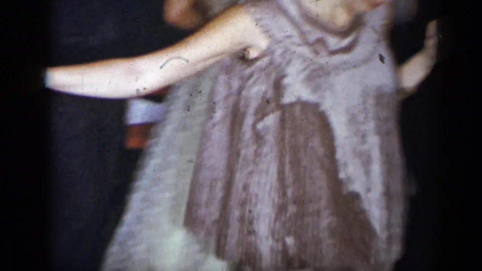 1954 New York home-movie frame of a woman in a light sleeveless dress extending her arm while dancing among party guests.