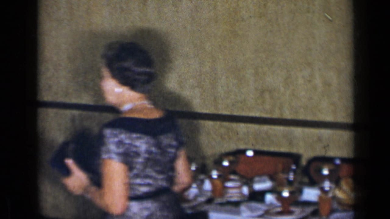 Woman in a patterned dress walking past a table during an indoor gathering.
