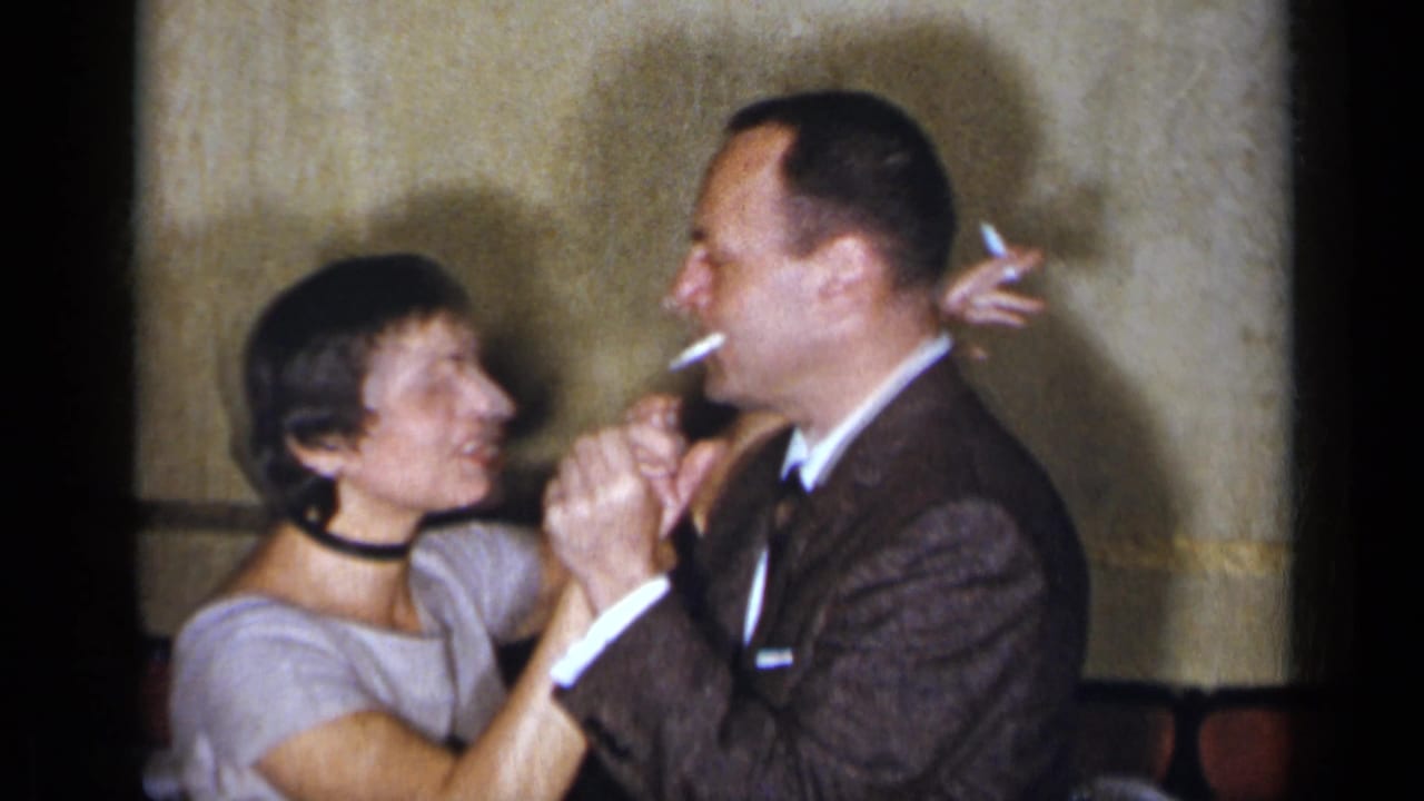 Man in a suit smokes while dancing closely with a woman in a light dress.