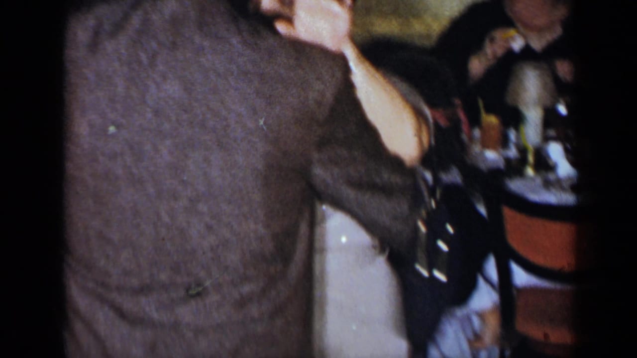 Adult in a brown jacket dancing beside seated party guests and a table.
