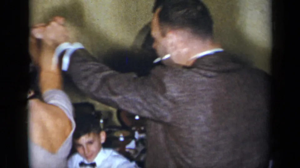 A couple dances closely in an indoor 1954 New York party frame, with another guest seated behind them.