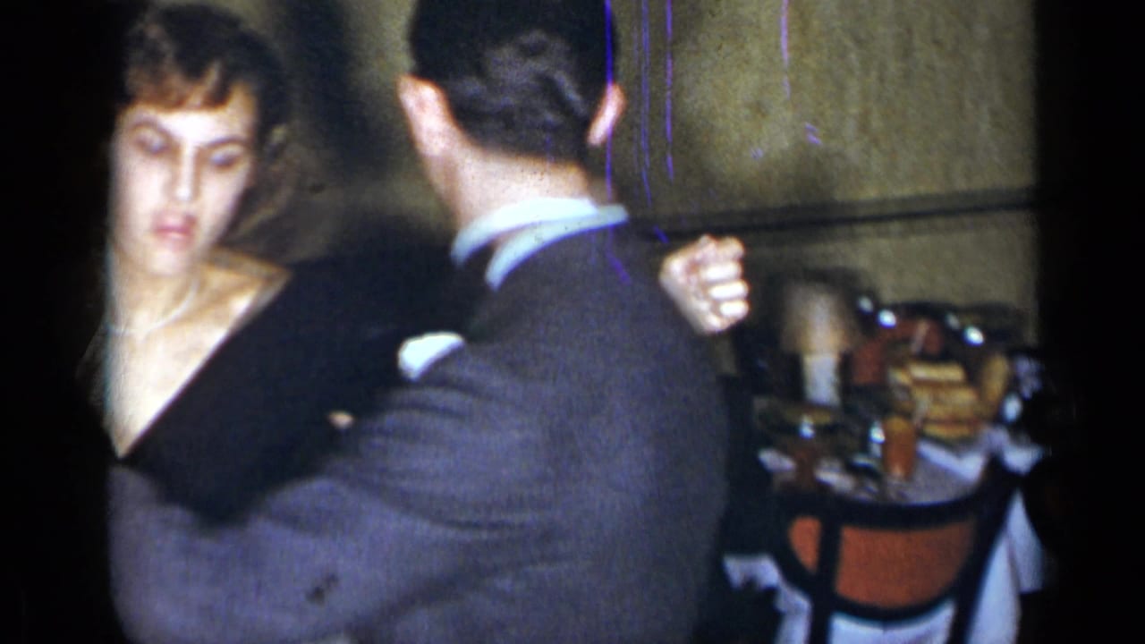 Woman in black dress dances with a man in a gray suit at an indoor gathering.